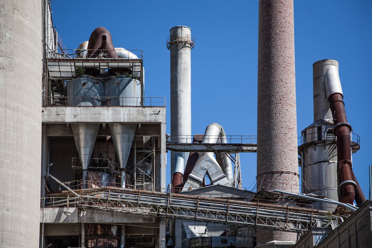 services-03 Close-up of a large industrial factory with concrete chimneys and metallic pipes against a clear blue sky.