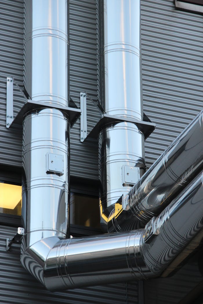 about-01 Close-up of shiny stainless steel pipes on an industrial building facade, showcasing modern technology.