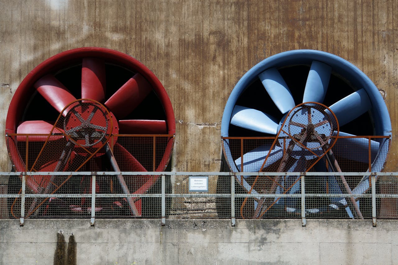 about-06 Close-up of large red and blue industrial fans on a rustic wall showcasing machinery and ventilation.
